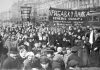 A demonstration of workers from the Putilov plant in Petrograd (modern day St. Peterburg), Russia, during the February Revolution. The left banner reads (misspelt) "Feed [plural imperative] the children of the defenders of the motherland"; the right banner, "Increase payments to the soldiers' families - defenders of freedom and world peace". Both refer to the economic toll the First World War was having on civilian life, February 1917 (probably around March 7 [O.S. February 22]) Photo: Unknown. Public Domain.
