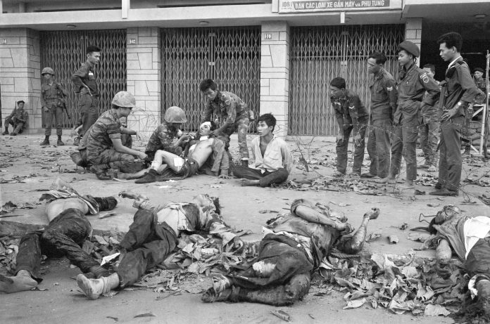 Tet Offensive, Saigon 1968. A Viet Cong prisoner sits next to corpses of 11 of his slain fellow guerrillas after a street fight in Saigon-Cholon on February 11, 1968. In the background are Vietnamese Marines that defeated a Viet Cong platoon holed up in the residential area. The prisoner was later taken out for interrogation. Photo: Eddie Adams/AP. (CC BY 2.0). Source: flickr.com