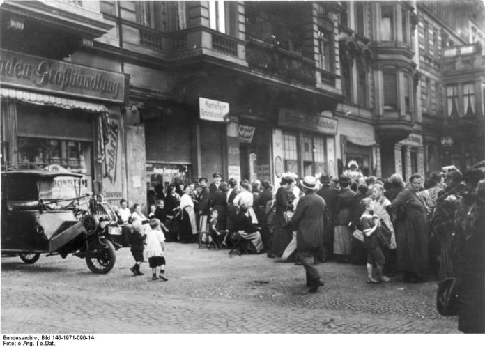 Distress of the 1920s. People stand in line in front of a shop. Photo: Unknown/German Federal Archives. (CC BY-SA 3.0 DE).
