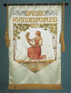 I kvindernes takketog til kongen i 1915 blev Dansk Kvindesamfunds banner båret forrest. Dansk Kvindesamfunds banner brugt ved landsmøderne frem til 1967. Motivet er tegnet af kunstneren Anna E. Munk, 1911.
