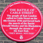 Red plaque commemorating The Battle of Cable Street. Location: Dock Street, near Cable Street junction, London, 17 Sept 2005. Photographer: Richard Allen. Public Domain.