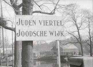 Jewish Ghetto in Amsterdam, Nederlands. WS street with large street sign: JUDEN VIERTEL JOODSCHE WIJK. 1942. See about the Dutch protests against persecutions of jews, January 25. 1941. Accessed at US Holocaust Memorial Museum, courtesy of Nederlands Instituut voor Beeld en Geluid.