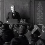 Professor George Brandes (1842-1927) holder forelæsning på Københavns Universitet. De studerende rejser sig høfligt før og efter forelæsningen. Fra en 1 minut lang stumfilm fra 1912.