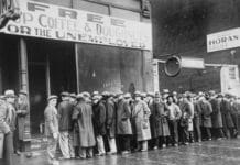 Unemployed men queued outside a depression soup kitchen opened in Chicago by Al Capone. The storefront sign reads "Free Soup Coffee & Doughnuts for the Unemployed." February 1931. Photo: Unknown author or not provided. Current location: National Archives at College Park, National Archives and Records Administration. Public Domain.