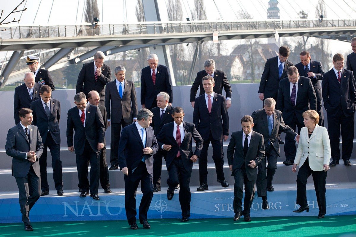 President Barack Obama, NATO Secretary General Jaap de Hoop Scheffer, Gordon Brown, Nicolas Sarkozy, Angela Merkel and other fellow NATO leaders step down from a photo platform April 4, 2009, following their group photo at the NATO meeting in Strasbourg, France on 4 April 2009. Photo: Official White House Photo by Pete Souza. (CC BY 2.0).