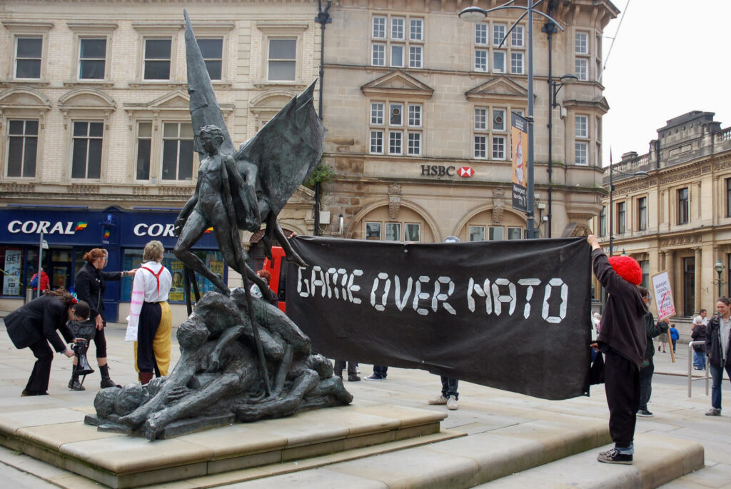Game over NATO banner at the chartist statue in Newport, Wales during a anti-NATO demonstration in 2014. Photo: Taken in 7 June, 2014 by Vertigogen. (CC BY-NC-SA 2.0).