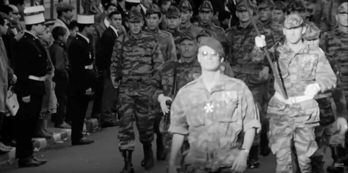 Scene fra filmen, hvor franske faldskærmstropper ankommer med obersten i spidsen, hyldet af folk fra den franske koloni i Algeriet. Skærmbillede fra filmen.