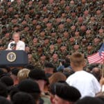 President George W. Bush addresses troops and families of the 10th Mountain Division and other members of the Fort Drum Community at Fort Drum, N.Y., July 19, 2002. Series: Photographs Related to the George W. Bush Administration, 1/20/2001 – 1/20/2009 Collection: Records of the White House Photo Office (George W. Bush Administration), 1/20/2001 – 1/20/2009. Public Domain.