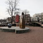 Amsterdam – Zwanenburgwal / Amstel – View West on Statue of Benedictus de Spinoza. Statue made 2008 by Nicolaas Lambertus Maria (Nicolas) Dings (1953-), Dutch sculptor and draughtsman. Photo: Taken 2008 by Txllxt TxllxT. (CC BY-SA 4.0).
