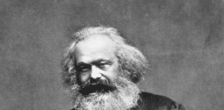 Photographic portrait of Karl Marx seated with a thumb in his lapel and his hand on his thigh, 1875. From: Reminiscences of Carl Schurz, Vol. I, New York: McClure Publ. Co., 1907, Chap. 4, facing p. 170. (This is the source of the first version only. Photo: John Jabez Edwin Mayal (1813–1901). Public Domain.