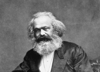 Photographic portrait of Karl Marx seated with a thumb in his lapel and his hand on his thigh, 1875. From: Reminiscences of Carl Schurz, Vol. I, New York: McClure Publ. Co., 1907, Chap. 4, facing p. 170. (This is the source of the first version only. Photo: John Jabez Edwin Mayal (1813–1901). Public Domain.