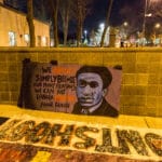 Banner outside the Minneapolis Police Department fourth precinct, Plymouth Avenue, following the officer-involved shooting of Jamar Clark on November 15, 2015. The quote says: “We revolt simply because for many reasons we can no longer breathe.” -Frantz Fanon. Photo by Tony Webster. (CC BY 2.0).