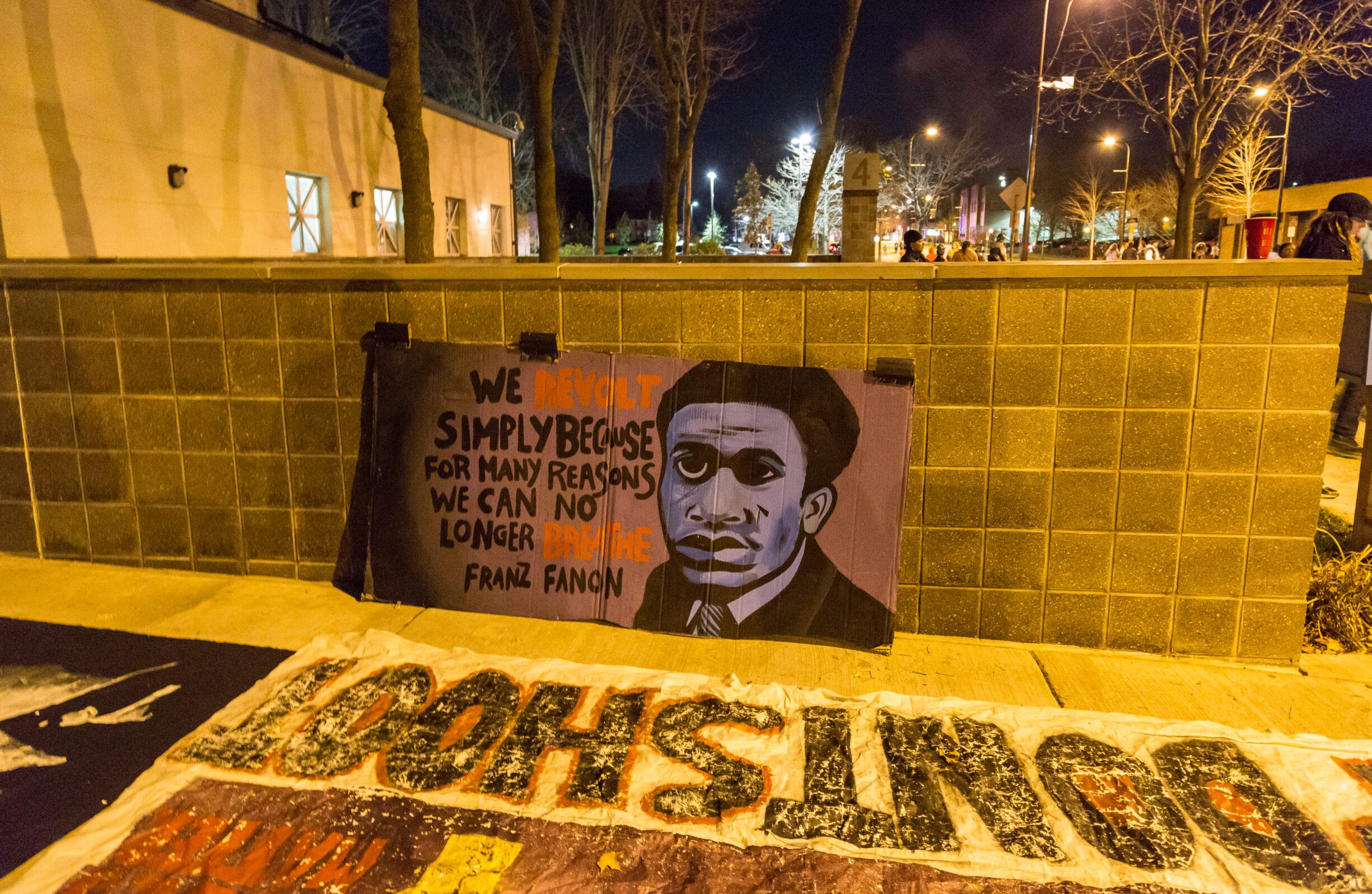 Banner outside the Minneapolis Police Department fourth precinct, Plymouth Avenue, following the officer-involved shooting of Jamar Clark on November 15, 2015. The quote says: "We revolt simply because for many reasons we can no longer breathe." -Frantz Fanon. Photo by Tony Webster. (CC BY 2.0).