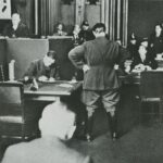 Speech by G. Dimitrov at the trial on the arson of the Reichstag, Leipzig, 1933. Goering is standing with his back. Source handwritten scan of the book World War II. Photo album / Comp. T. Bushueva, V. Drugov, A. Savin, art director N. Pyanykh. – M.: Planet, 1989. Photo: unknown, not specified in source. Public Domain.