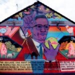 A mural in Ardoyne, Belfast, Northern Ireland featuring Malcolm X. The mural was destroyed soon after painting and no longer exists. It was painted by American artist Mike Alewitz in 2002. Alewitz chose Malcolm X for the mural as there had been tensions in Ardoyne about catholic children attending a protestant school, recollecting the struggle to racially integrate schools in the Civil Rights era in the United States. The mural was destroyed by Sinn Fein during a period of negotiation with Loyalists in Northern Ireland in an attempt to reduce sources of tension between the two groups. 23 July 2002. (CC BY-SA 4.0).