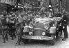 Parade of SA troops past Hitler, Nuremberg 1935. In the car with Hitler: the Blutfahne, behind the car: SS-man en:Jakob Grimminger the carrier of the Blutfahne flag. From the Reichsparteitag der NSDAP 10th-16th September 1935. Author: Charles Russell Collection, NARA. Public Domain. Source: Wikimedia Commons