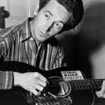 Woody Guthrie playing a guitar that has a sticker attached reading: This Machine Kills Fascists. Photo: Taken 8 March 1943 by Al Aumuller. Collection: New York World-Telegram and the Sun, Library of Congress. Public Domain.