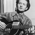 Woody Guthrie with his guitar. Photo: Taken 8 March 1943 by Al Aumuller. Collection: New York World-Telegram and the Sun, Library of Congress. Public Domain.