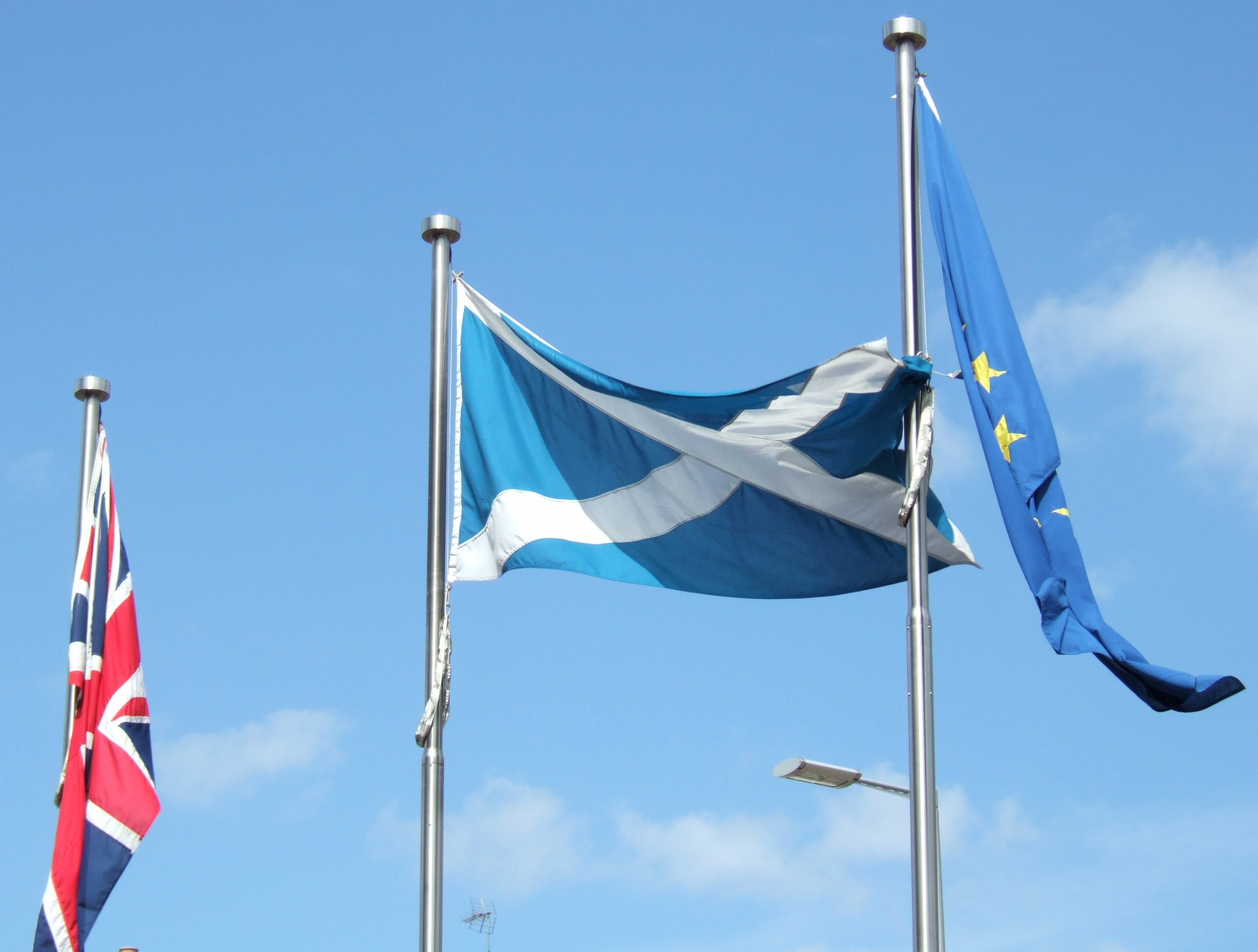The Scottish flag between the British and The European Union flags outside the Scottish Parliament in Edinburgh, Scotland. Photo: Taken 13 June 2006 by Calum Hutchinson. (CC BY-SA 2.5).